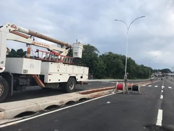 Caminhão com cesto aéreo instalando poste de iluminação pública em avenida