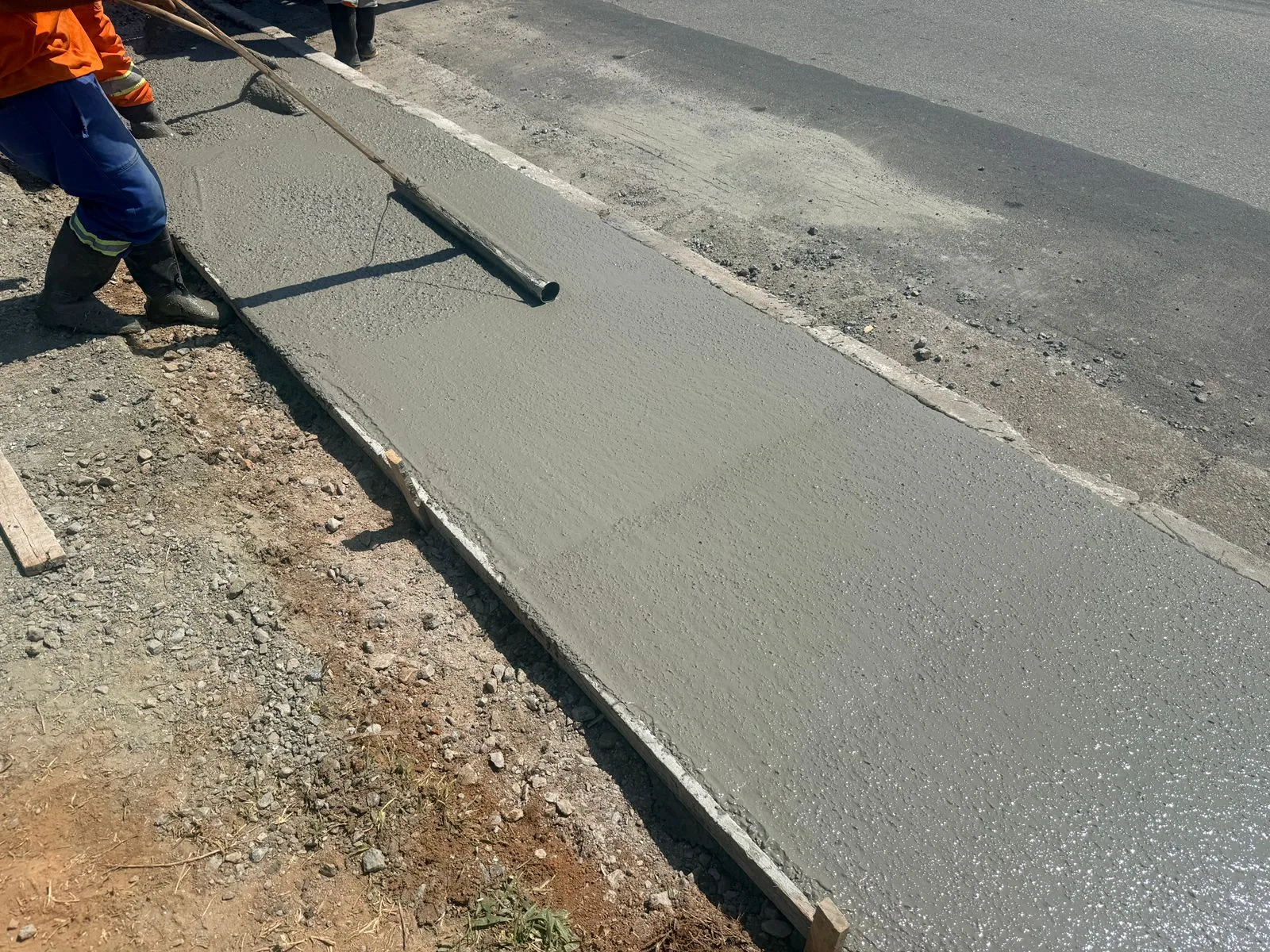 Passeio de concreto recém-concretado ao lado da guia e da pista asfaltada