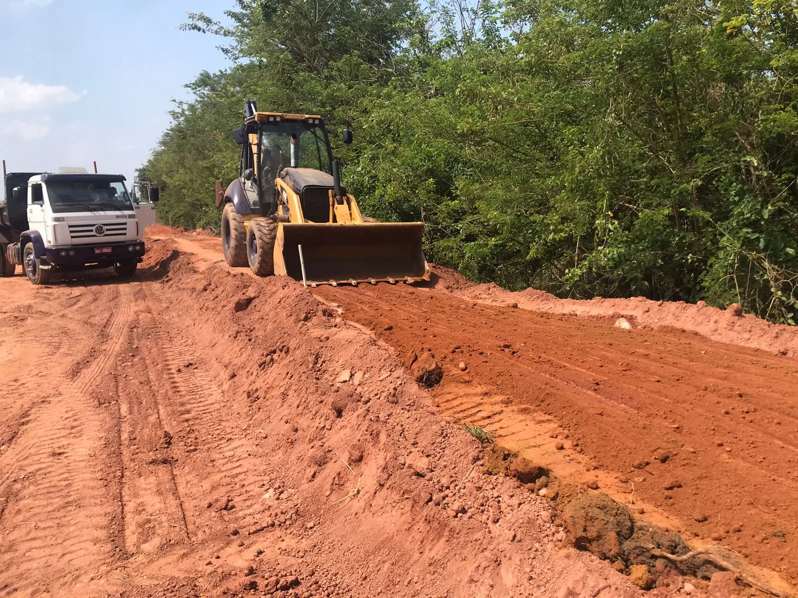 Retroescavadeira e caminhão basculante em serviço de terraplenagem em estrada de terra